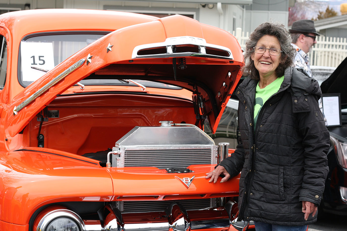 Woman smiling standing next to orange classic truck with the hood open